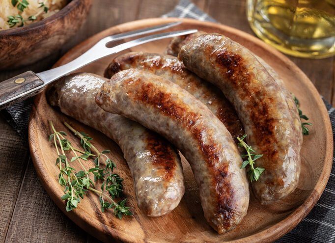 A wooden plate with three sausage links on it.