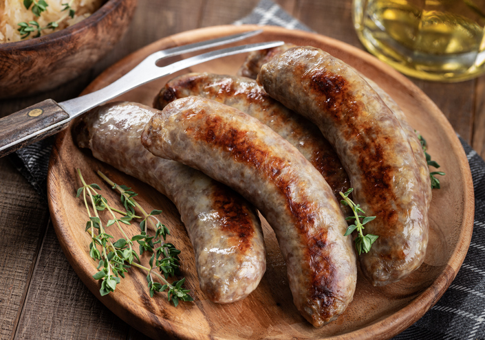 A wooden plate with three sausage links on it.