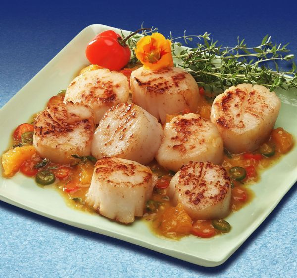 A plate of scallops with tomato sauce and herbs.